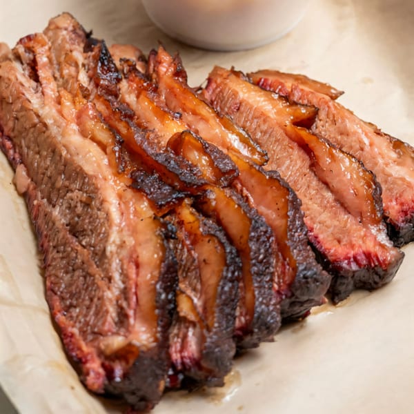 Close-up of sliced, juicy BBQ brisket with a dark, smoky crust on parchment paper.