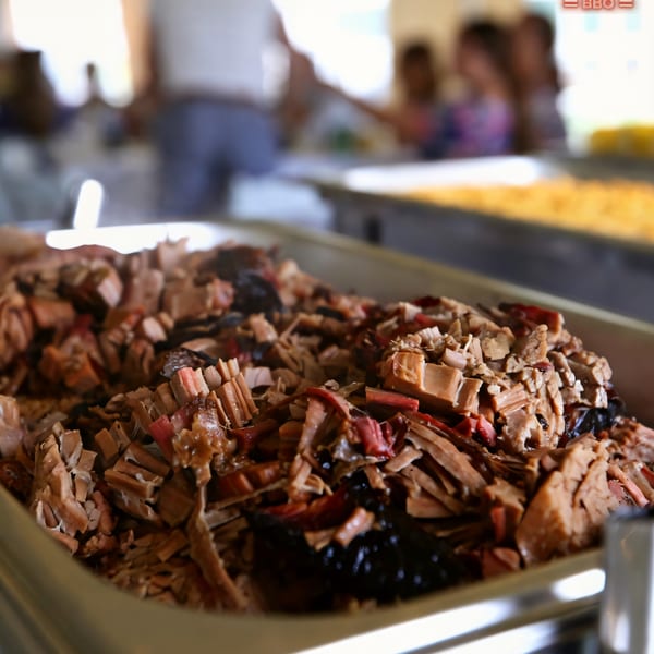 Close-up of a large tray of Baby Back Blues BBQ pulled pork, with blurred people in background.
