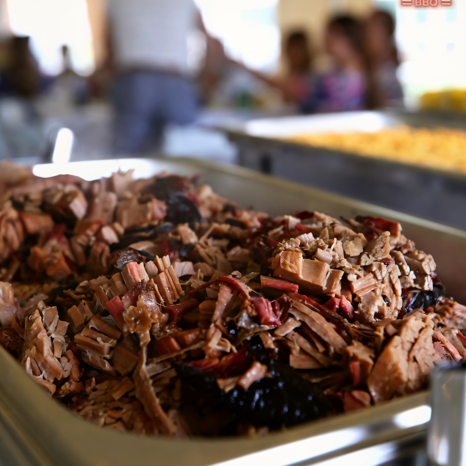 Close-up of a large tray of Baby Back Blues BBQ pulled pork, with blurred people in background.