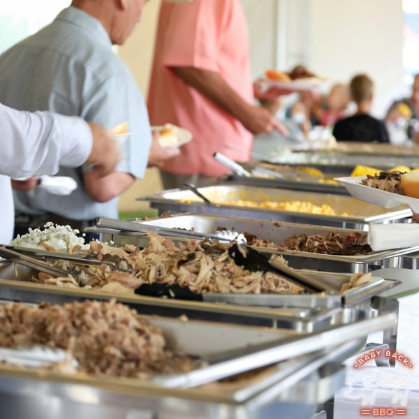 People serving themselves from a Baby Back Blues BBQ buffet line with pulled pork and sides.