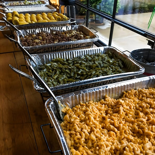 A buffet line of BBQ sides, including mac and cheese, green beans, and corn on the cob.