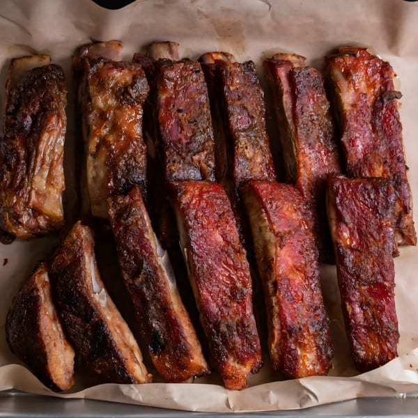Rows of glistening, saucy Baby Back Blues BBQ ribs on brown parchment paper in a metal tray.