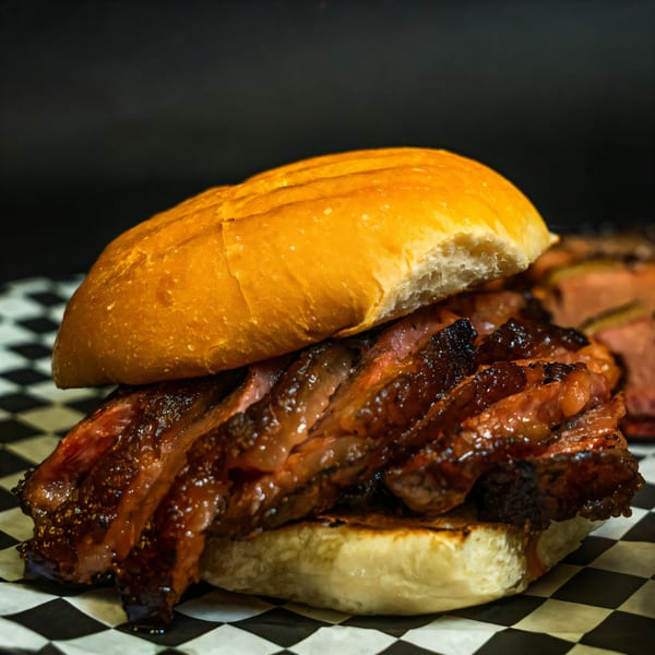 Close-up of a Baby Back Blues BBQ brisket sandwich on a checkered paper liner.